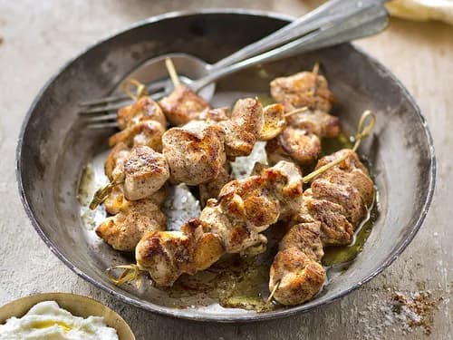 Brochettes de chich taouk grillées, poulet doré mariné au yaourt et aux épices, servies avec un bol de sauce toum blanche et des quartiers de citron.
