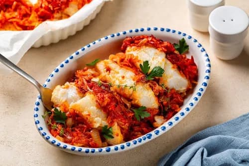 Psari plaki, filets de poisson blanc cuits au four à la grecque sur un lit de pommes de terre fondantes, nappés de sauce tomate, rondelles de citron et persil frais.