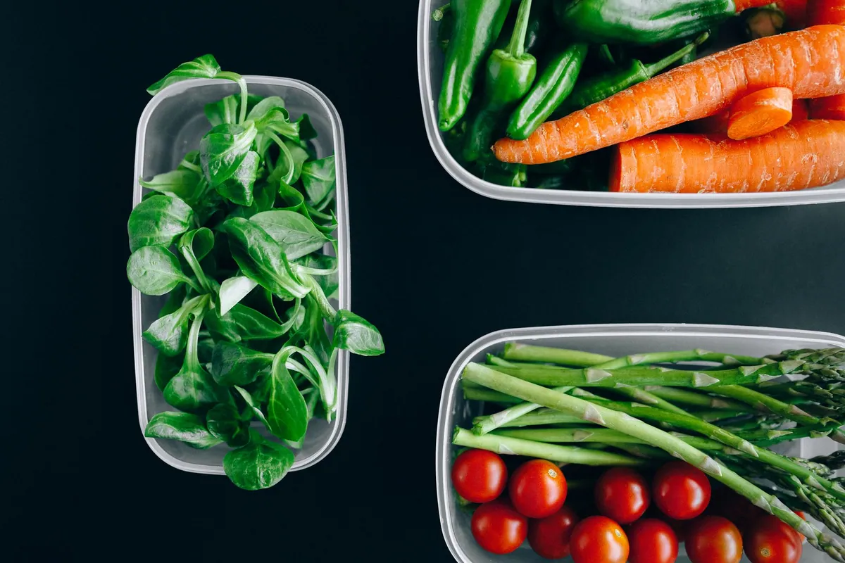 Plan de travail avec plusieurs repas de la semaine préparés dans des boîtes, entourés de légumes frais