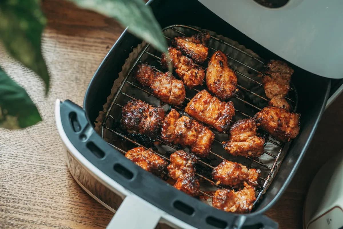 Panier d'air fryer ouvert sur un plan de travail, garni de morceaux de légumes et de poulet dorés en une seule couche