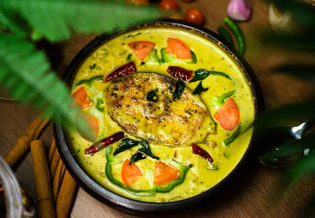Curry de poisson du Kerala dans une sauce au lait de coco, garni de feuilles de curry fraîches, servi avec du riz blanc