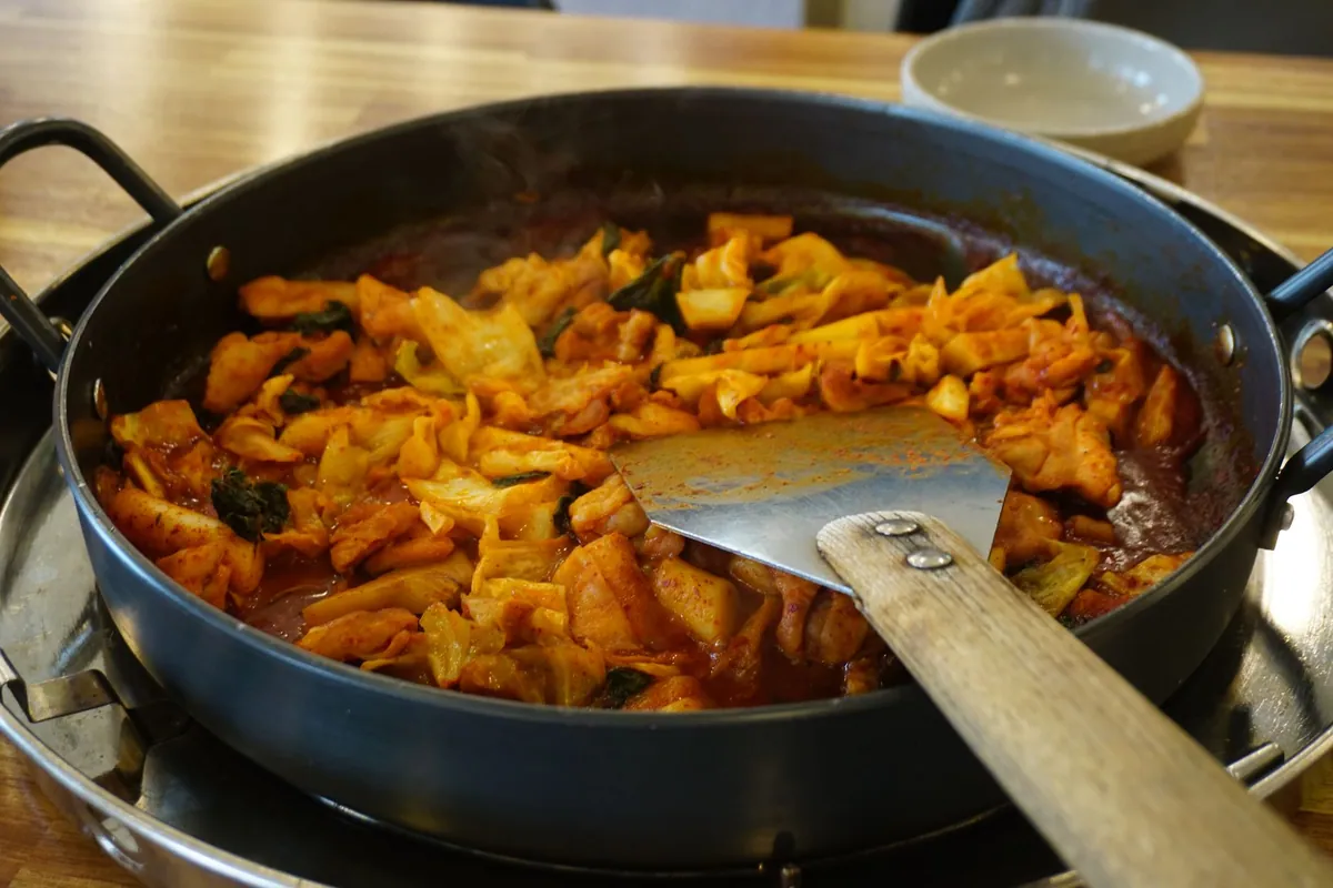Bouchées de dak-gangjeong, poulet frit coréen doublement cuit et enrobé de sauce brillante au gochujang, parsemées de cacahuètes concassées et de graines de sésame.