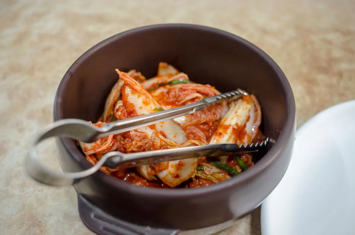 Ttukbaegi de kimchi jjigae bouillonnant avec porc, tofu et kimchi, servi avec un bol de riz blanc.