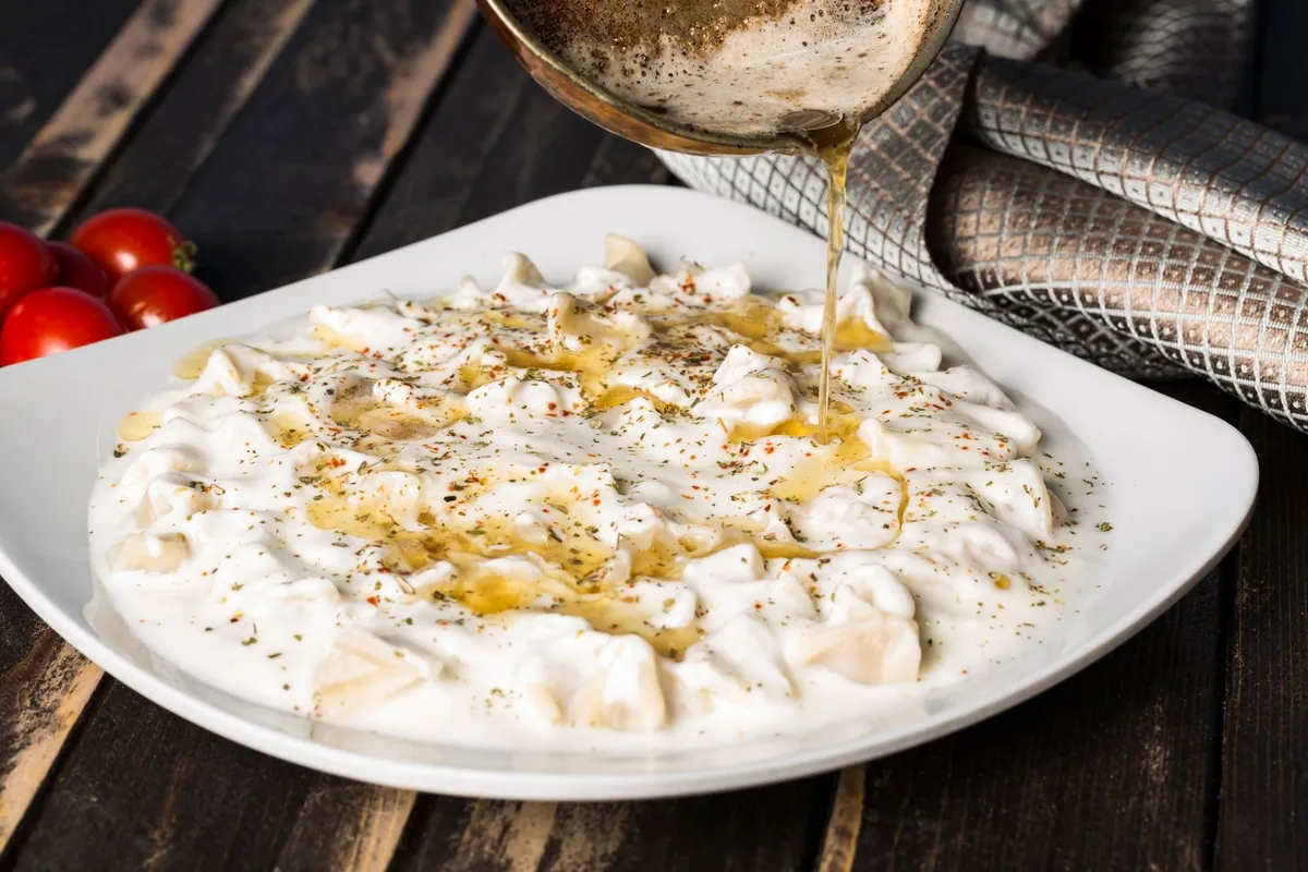 Assiette de manti turcs faits maison nappés de yaourt à l'ail et de beurre fondu au piment rouge, parsemés de menthe séchée
