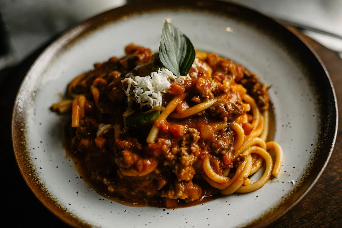 Assiette de pasta alla Norma avec rigatoni nappés de sauce tomate, dés d'aubergine frits, copeaux de ricotta salata et feuilles de basilic frais