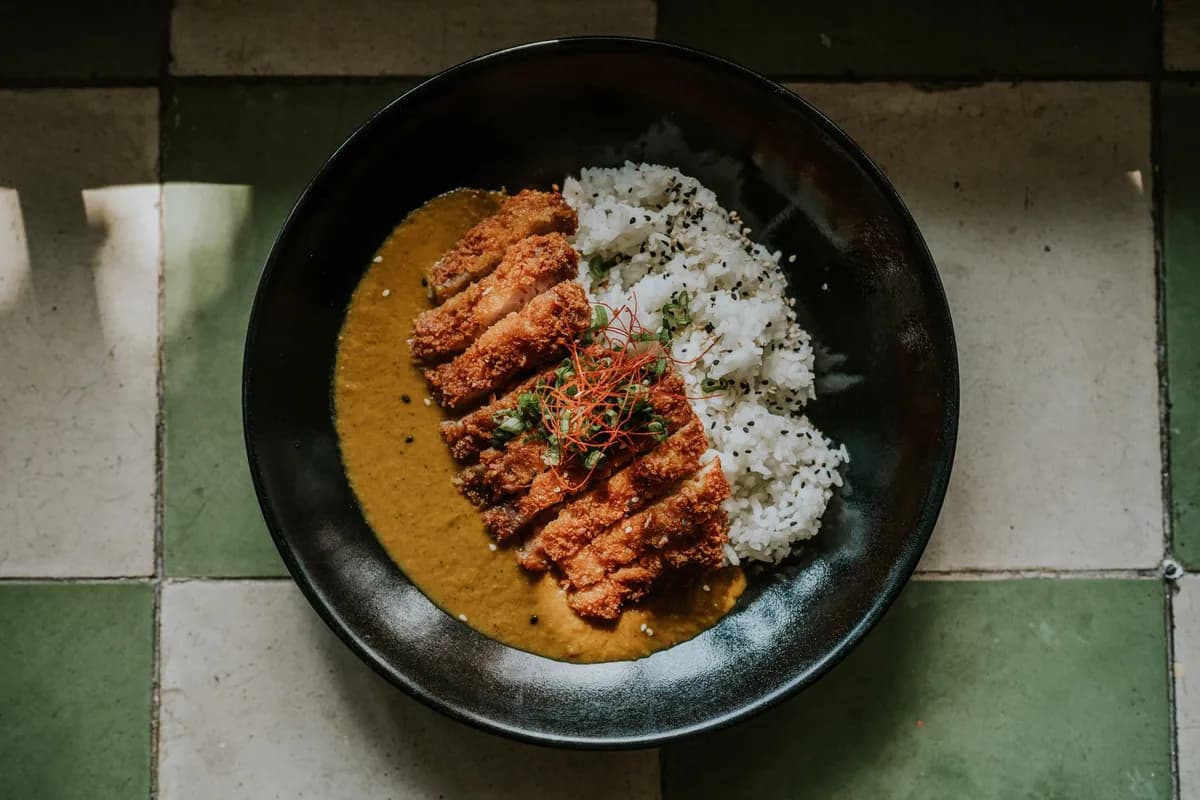 Poulet katsu curry : escalope de poulet panée au panko tranchée en lanières, dressée sur un riz japonais nappé de curry doux et épais, dans une assiette creuse.