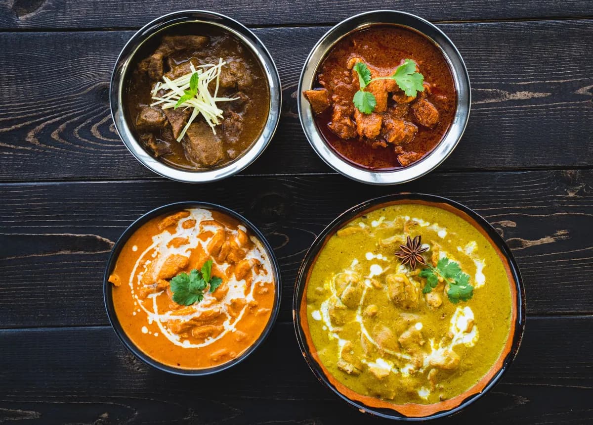 Brochettes de poulet tikka masala grillées puis nappées d'une sauce tomate crémeuse orangée, parsemées de coriandre fraîche, servies avec du riz basmati et un naan doré.