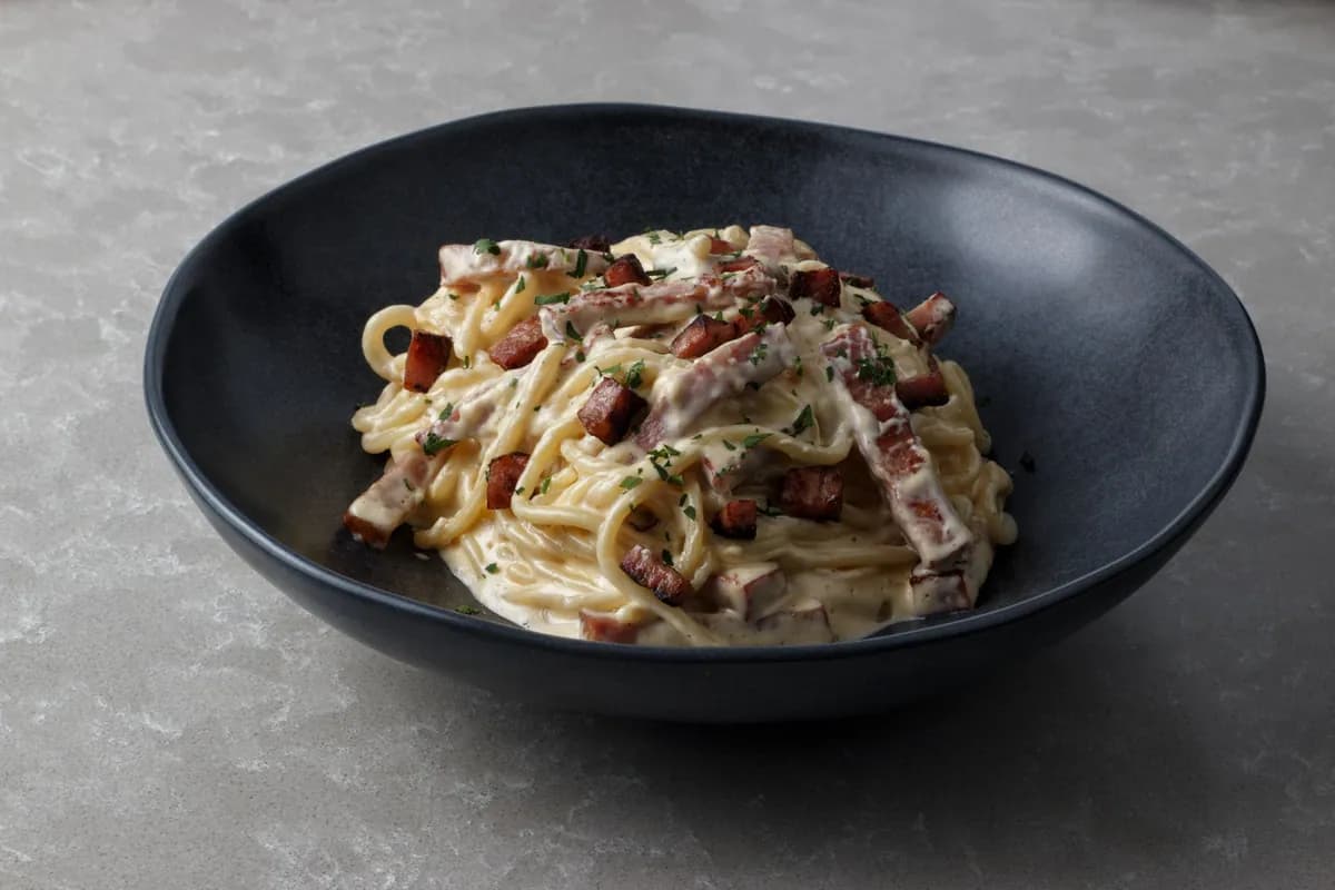 Assiette de spaghetti alla carbonara nappés d'une sauce crémeuse aux jaunes d'œufs et pecorino, parsemés de dés de guanciale doré et de poivre noir moulu.