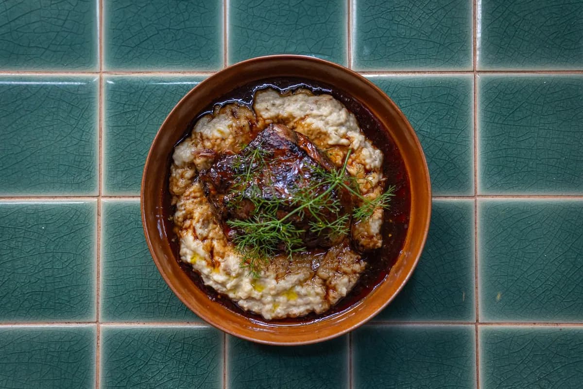 Youvetsi d'agneau au four dans une cocotte en fonte, orzo kritharaki nappés de jus tomaté à la cannelle, agneau fondant et kefalotyri râpé, plat grec traditionnel.