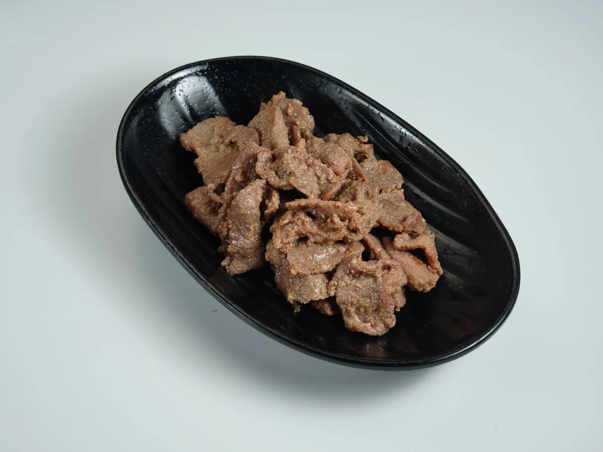 Lamelles de bœuf bulgogi caramélisées dans une poêle en fonte, parsemées d'oignons nouveaux et de graines de sésame, servies avec du riz vapeur et des feuilles de salade.