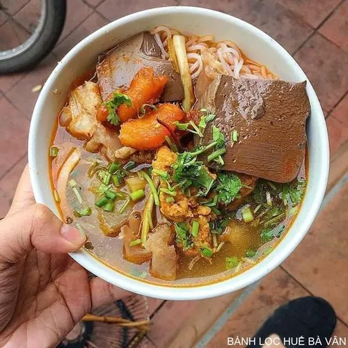 Bol de bún bò Huế avec bouillon rouge épicé, nouilles de riz rondes, tranches de bœuf et de porc, garni d'herbes fraîches, de germes de soja et de citron vert.