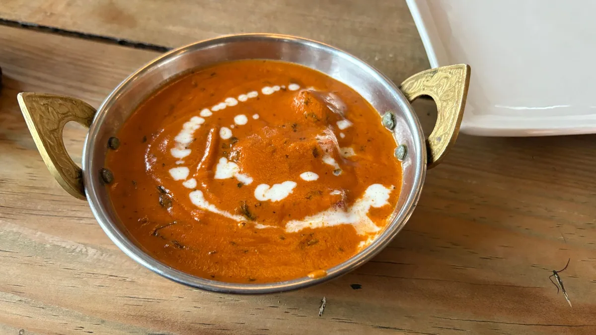 Bol de butter chicken (murgh makhani) fumant, poulet tendre dans une sauce tomate orangée au beurre et à la crème, garni de coriandre fraîche, servi avec un naan doré et du riz basmati.