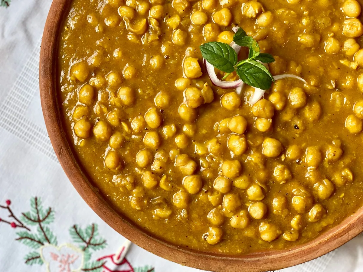 Chana masala servi dans un bol, sauce tomate épicée et pois chiches, parsemé de coriandre fraîche et d'oignon rouge, avec un bhatura à côté