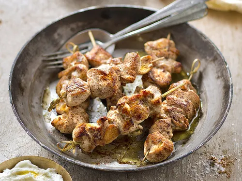 Brochettes de chich taouk grillées, poulet doré mariné au yaourt et aux épices, servies avec un bol de sauce toum blanche et des quartiers de citron.