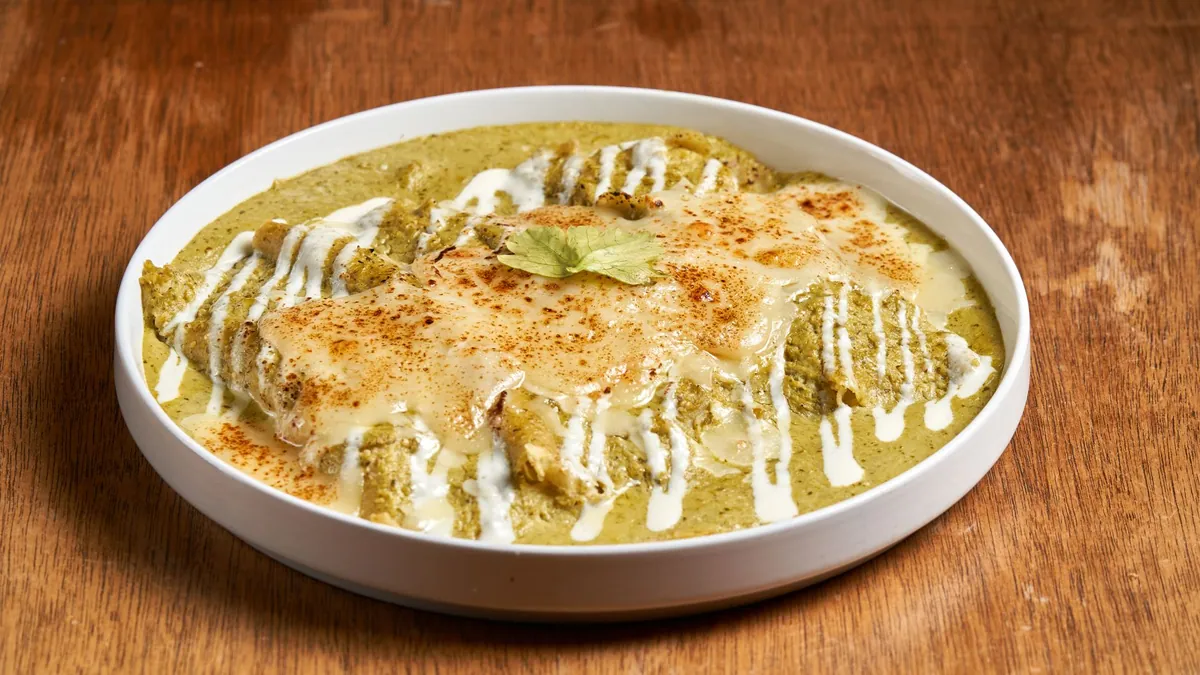 Chilaquiles verdes dans une assiette creuse : tortillas de maïs frites nappées de salsa verte, crème, queso fresco émietté, oignon rouge, coriandre fraîche et œuf au plat au jaune coulant.