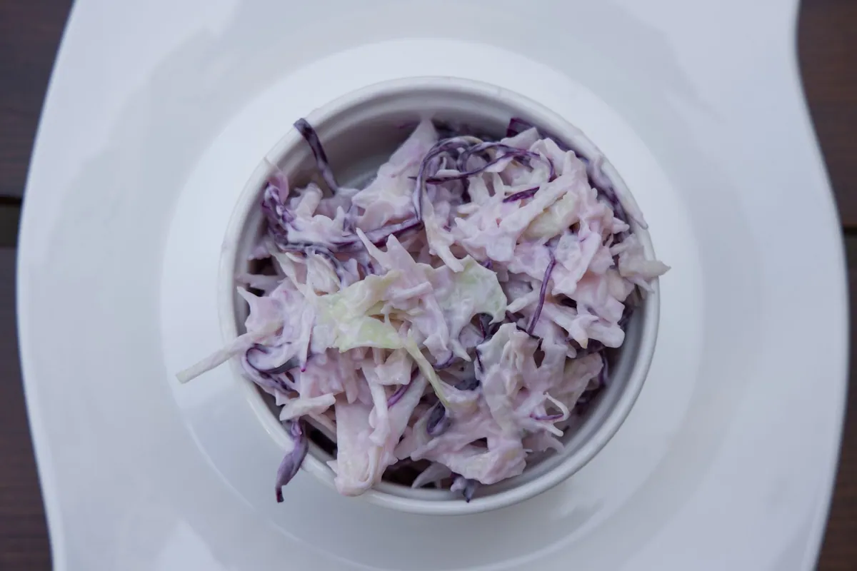 Coleslaw maison dans un bol, chou blanc et carottes finement émincés nappés d'une sauce crémeuse, servie en accompagnement de barbecue américain.