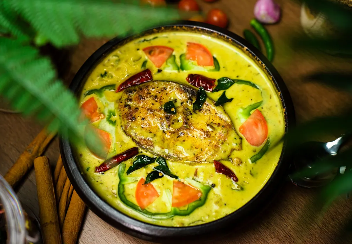 Curry de poisson du Kerala dans une sauce au lait de coco, garni de feuilles de curry fraîches, servi avec du riz blanc