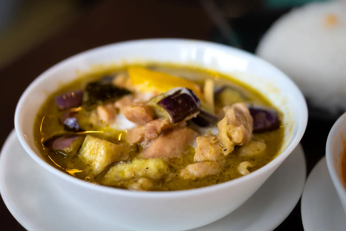 Bol de curry vert de poulet thaïlandais (kaeng khiao wan), sauce coco parsemée de basilic thaï et de piment rouge, aubergines thaïes, servi avec du riz jasmin vapeur.