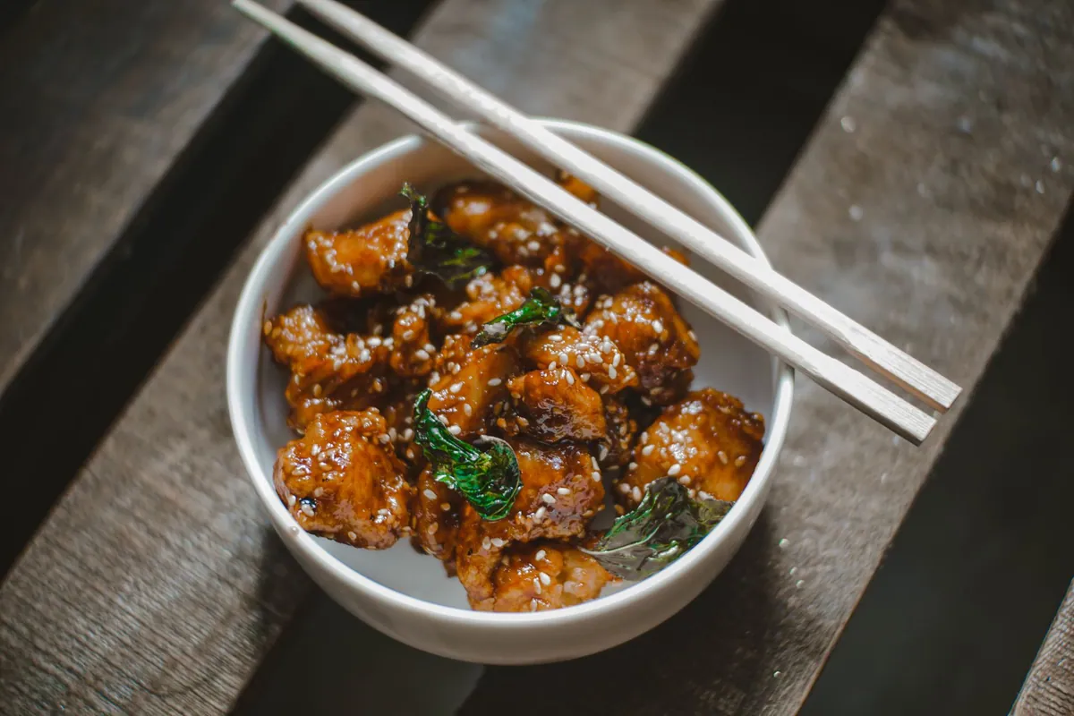 Bouchées de dak-gangjeong, poulet frit coréen doublement cuit et enrobé de sauce brillante au gochujang, parsemées de cacahuètes concassées et de graines de sésame.
