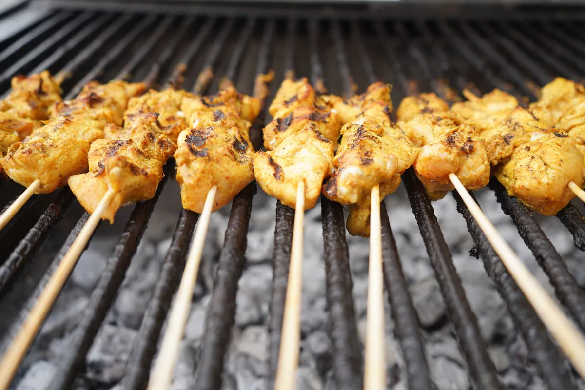 Cuisses de poulet vietnamien grillées et laquées à la citronnelle (gà nướng sả), dorées sur un barbecue, servies avec du riz blanc et des herbes fraîches.