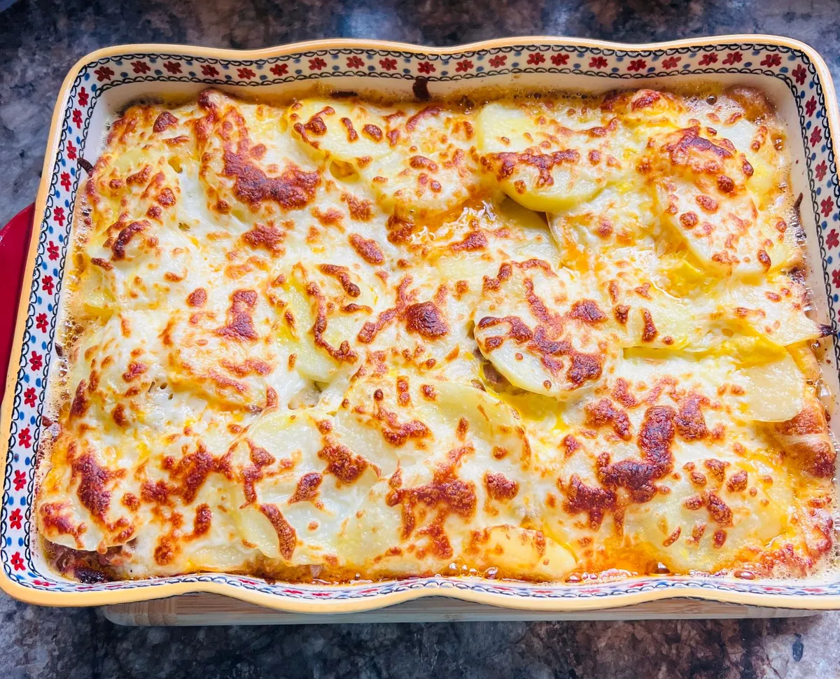 Gratin dauphinois doré dans son plat, une portion prélevée révélant les fines couches de pommes de terre fondantes nappées de crème.
