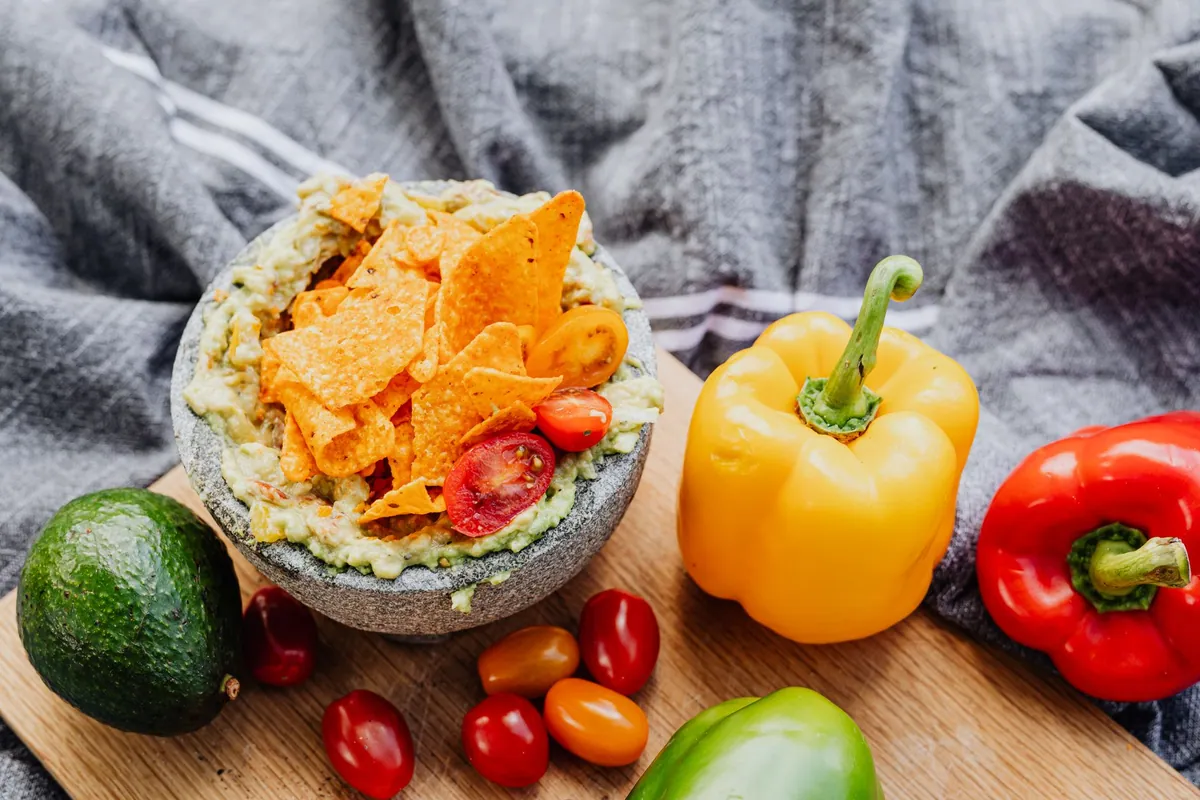 Bol de guacamole fait maison dans un molcajete en pierre, garni de coriandre fraîche et de dés de tomate, servi avec des totopos croustillants.