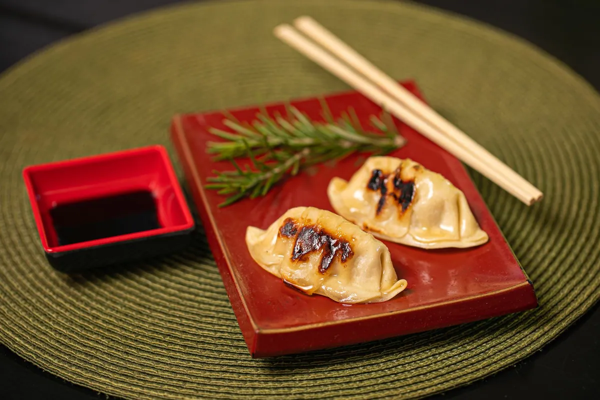 Gyoza au porc dorés et croustillants dessous, dressés en éventail dans une poêle, servis avec une sauce soja-vinaigre de riz