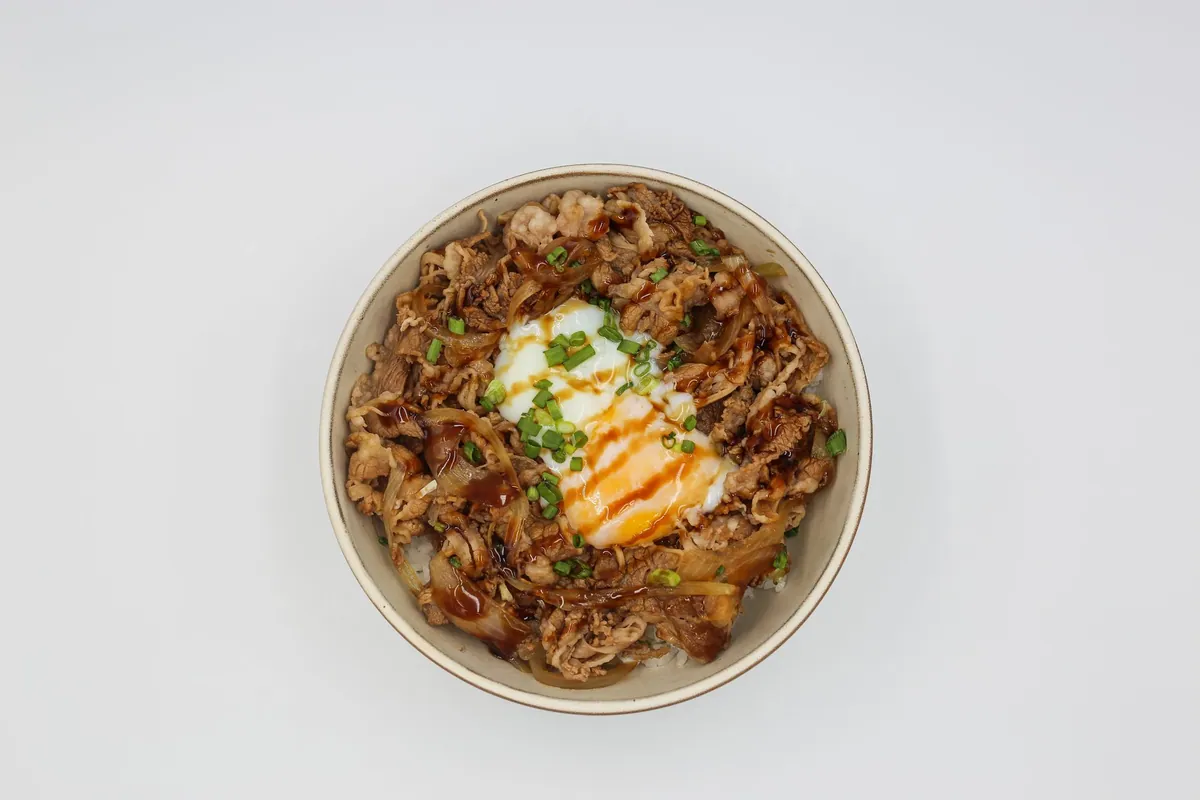 Bol de gyudon japonais avec fines lamelles de bœuf et oignons mijotés sur riz blanc, garni de ciboule fraîche et d'un jaune d'œuf.