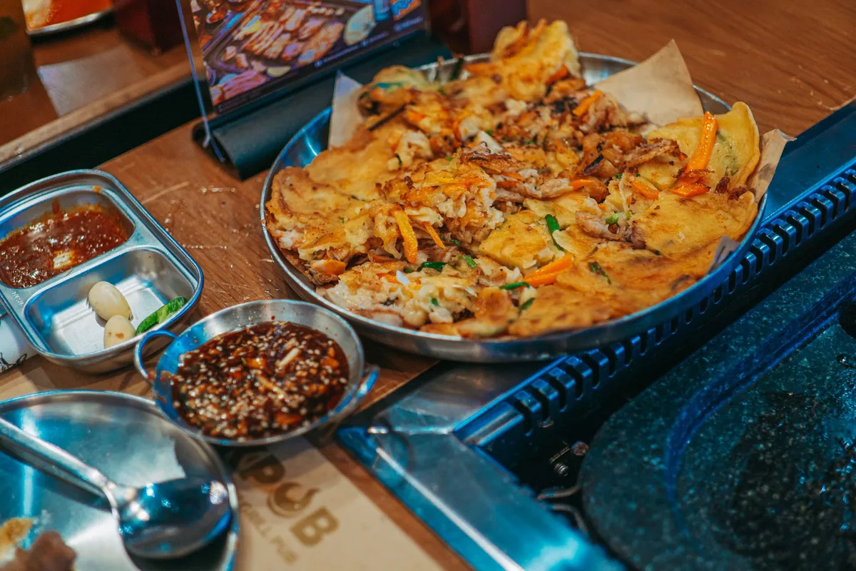 Haemul pajeon doré et croustillant garni de calamars, crevettes et oignons nouveaux, coupé en parts et servi avec une sauce soja-vinaigre.