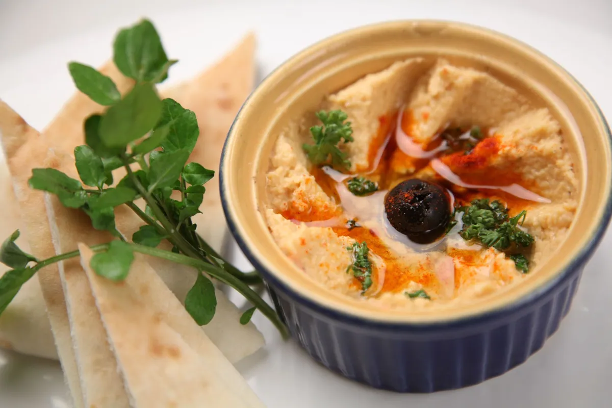 Bol de houmous libanais avec un puits d'huile d'olive au centre, saupoudré de paprika et de pois chiches entiers, servi avec du pain pita chaud.