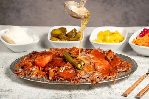 Assiette d'İskender kebab avec lamelles d'agneau grillé sur dés de pain pide, sauce tomate, beurre noisette doré et quenelle de yaourt