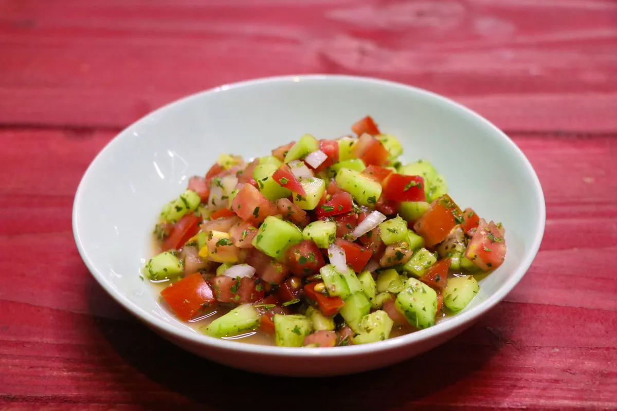 Kachumber, salade indienne de tomate, concombre et oignon rouge en dés, assaisonnée de citron vert, cumin torréfié et coriandre fraîche, servie dans une coupelle.