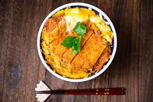 Bol de katsudon japonais avec tonkatsu de porc pané croustillant, œuf mollet, oignons fondants et riz blanc, servi dans un bol à donburi traditionnel.