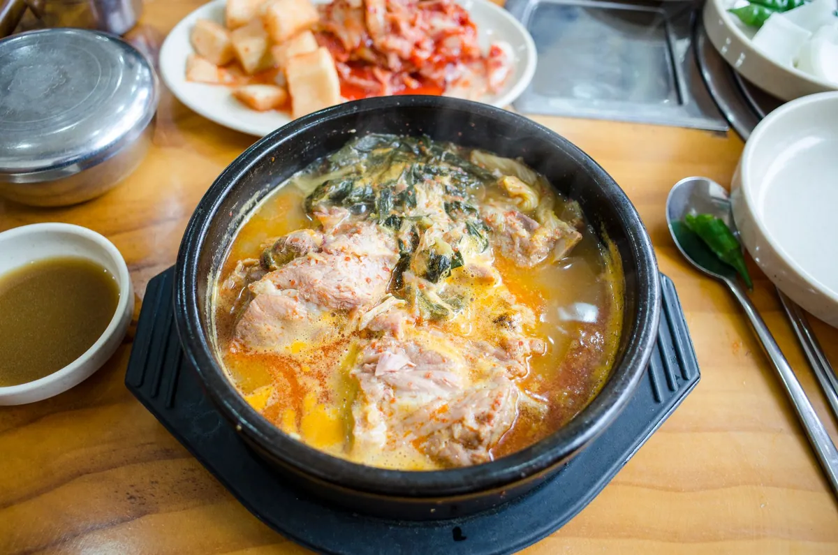 Ttukbaegi de kimchi jjigae bouillonnant avec porc, tofu et kimchi, servi avec un bol de riz blanc.