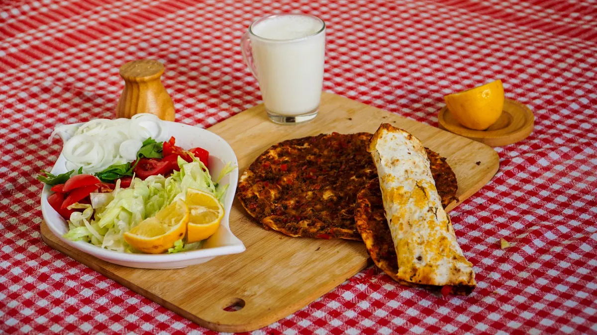 Lahmacun tout juste sorti du four, pâte fine et croustillante garnie de viande hachée épicée, servi avec quartiers de citron, persil frais et oignon émincé.