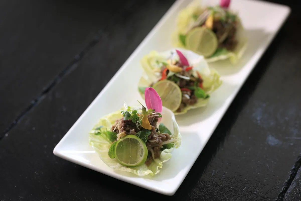 Larb gai, salade thaïlandaise tiède de poulet haché aux herbes fraîches, citron vert et riz grillé moulu, servie avec du riz gluant