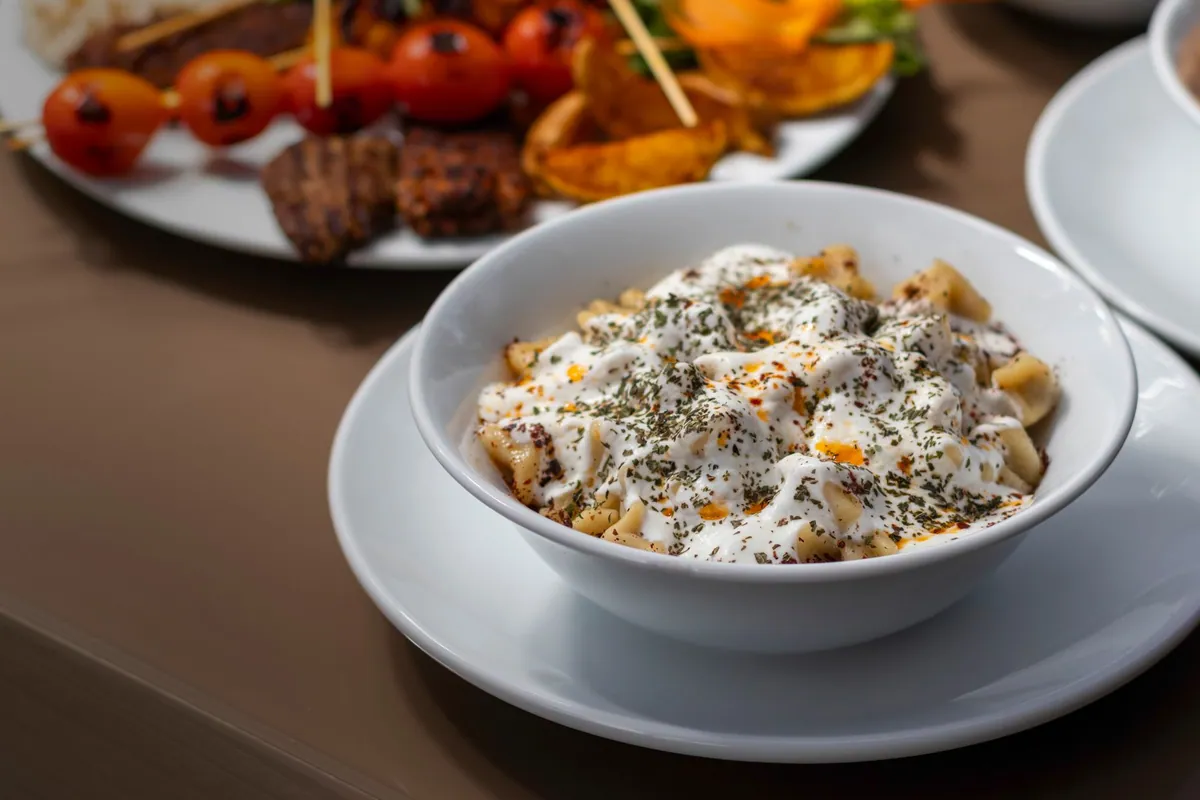 Assiette de manti turcs faits maison nappés de yaourt à l'ail et de beurre fondu au piment rouge, parsemés de menthe séchée