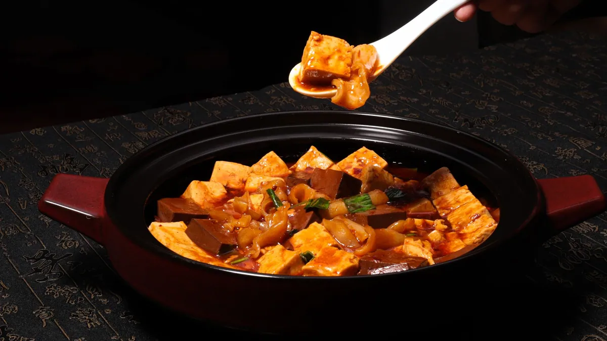 Bol de mapo tofu fumant, cubes de tofu soyeux nappés d'une sauce rouge piquante, parsemé d'oignons nouveaux et de poivre du Sichuan concassé