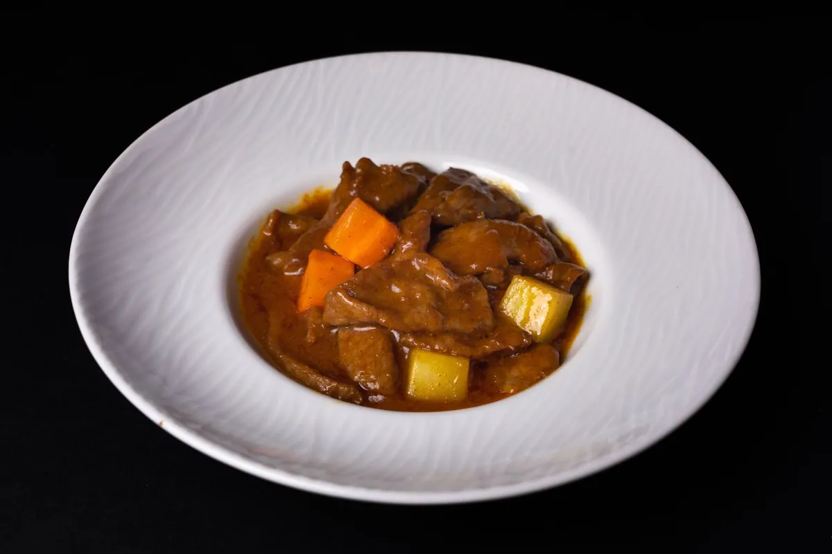 Curry massaman de bœuf thaïlandais dans un bol creux, sauce au lait de coco épaisse, pommes de terre fondantes et cacahuètes concassées, riz jasmin vapeur servi à part.