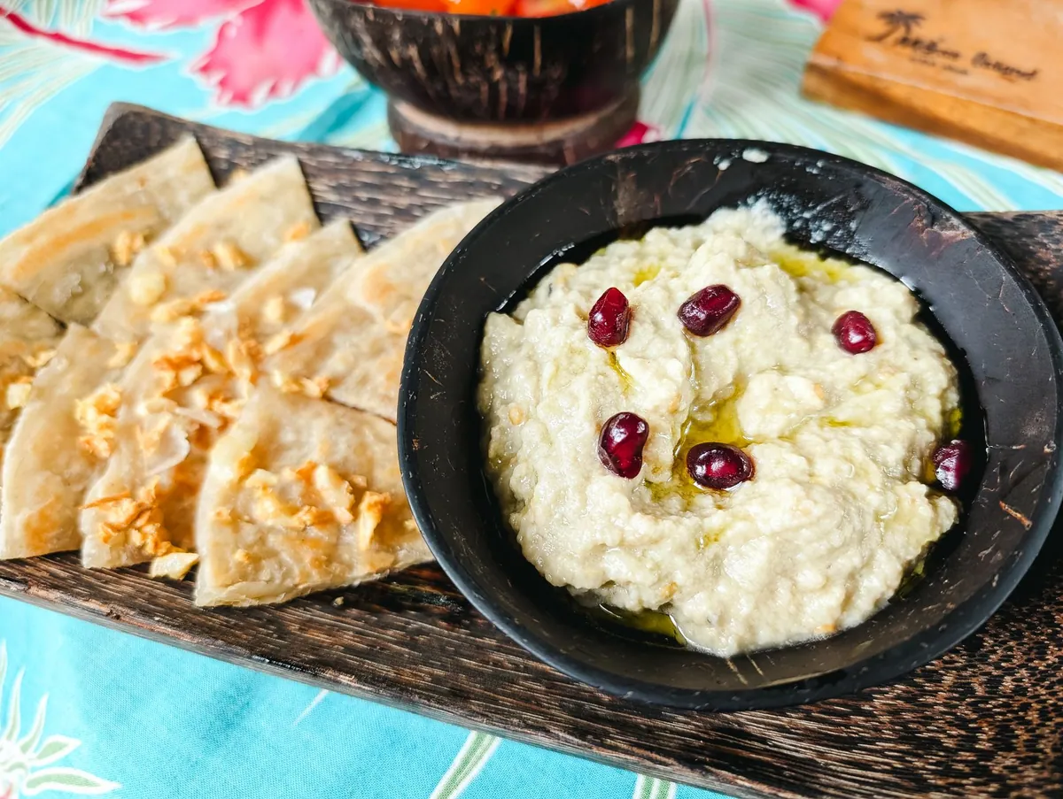 Moutabal libanais, caviar d'aubergine fumé nappé d'huile d'olive, parsemé de persil ciselé et de grains de grenade, servi avec du pain pita.