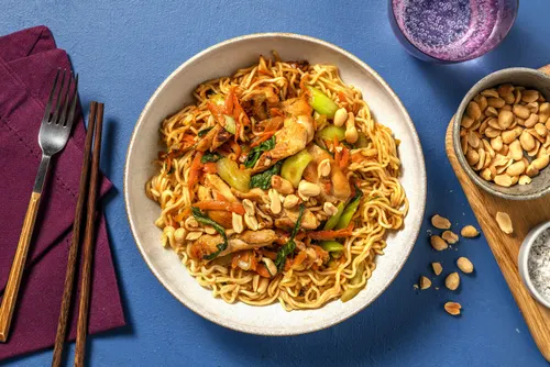 Chow mein au poulet dans un wok : nouilles chinoises dorées, poulet, carotte en julienne, chou chinois et germes de soja, parsemés d'oignons nouveaux et de sésame.