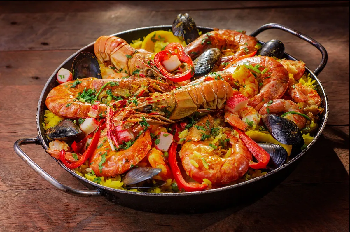 Paella valenciana traditionnelle au poulet et au lapin dans sa paellera en fer, riz bomba safrané avec socarrat doré au fond, servie à table.