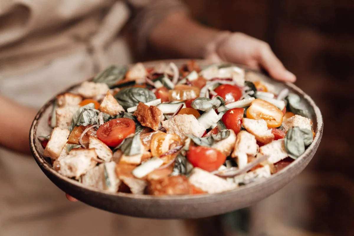 Panzanella toscane dans un saladier : cubes de pain de campagne, tomates mûres, concombre, oignon rouge et basilic frais, assaisonnés d'huile d'olive et de vinaigre de vin rouge.