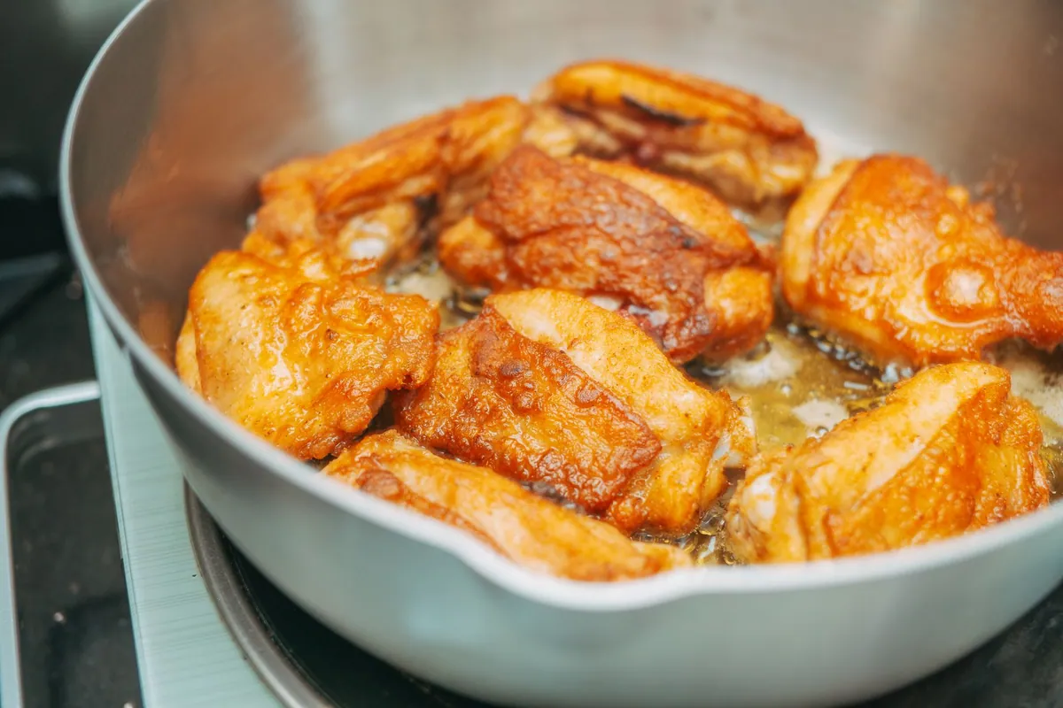 Morceaux de pollo al ajillo dorés avec gousses d'ail en chemise et sauce au vin blanc dans une cocotte, plat espagnol traditionnel parsemé de persil frais.