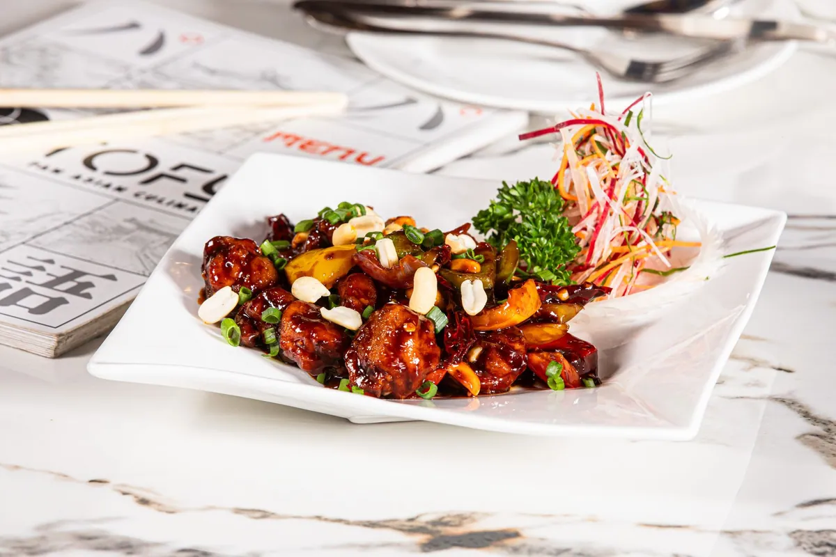 Poulet Kung Pao dans un wok, dés de poulet laqués de sauce brillante, piments rouges séchés, poivre du Sichuan et cacahuètes grillées, parsemés d'oignons nouveaux