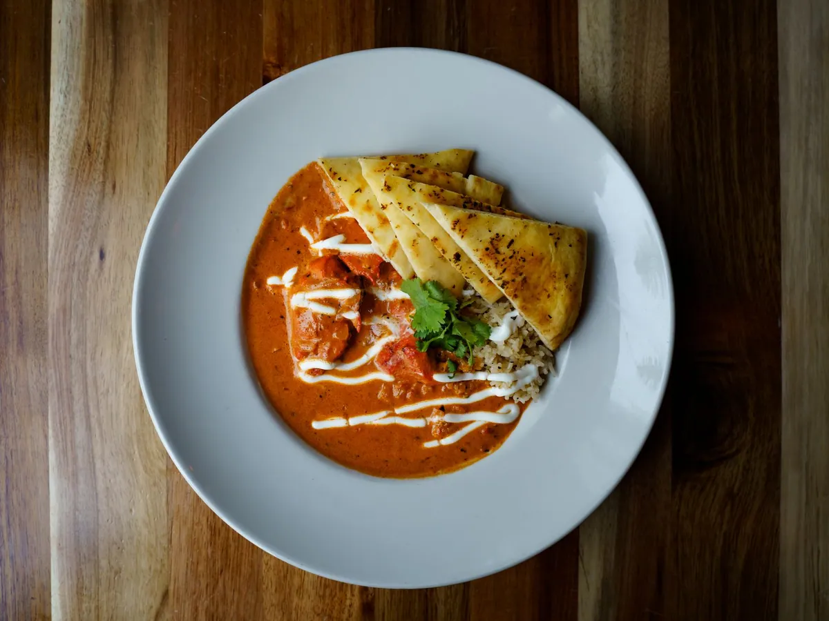 Brochettes de poulet tikka masala grillées puis nappées d'une sauce tomate crémeuse orangée, parsemées de coriandre fraîche, servies avec du riz basmati et un naan doré.