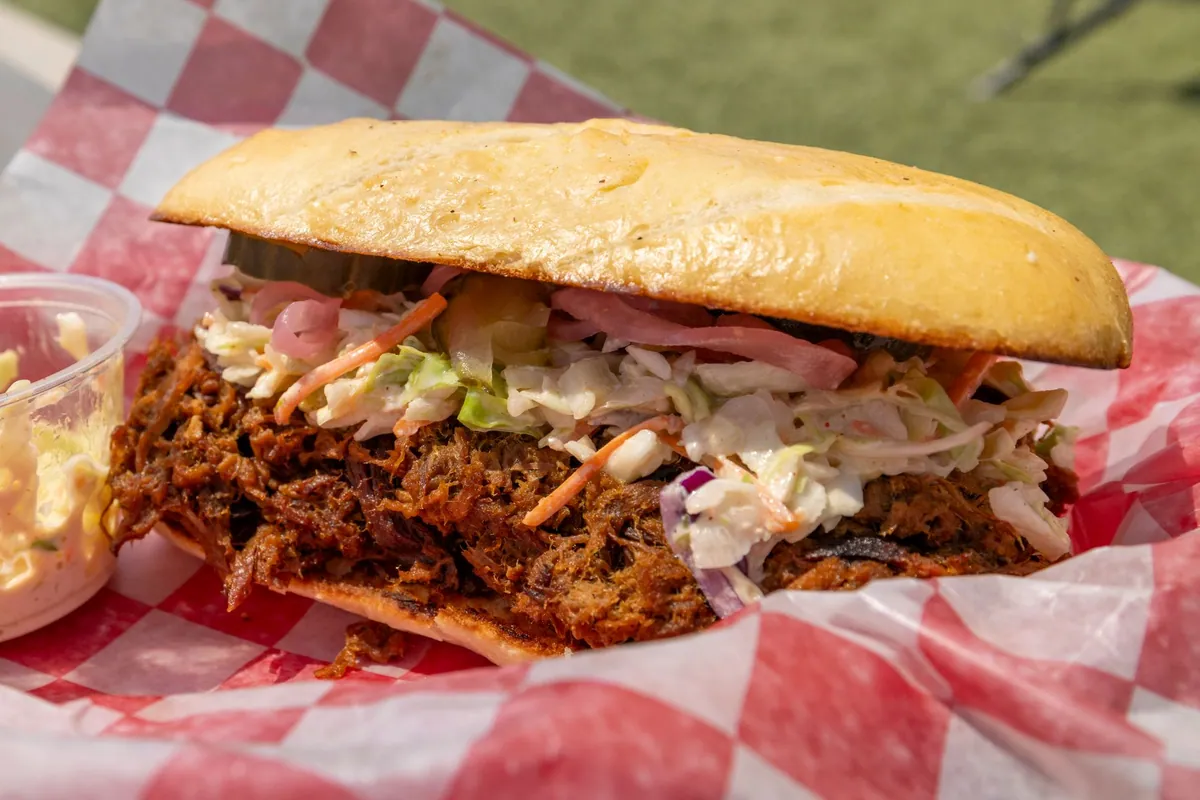 Porc effiloché façon pulled pork BBQ nappé de sauce barbecue, servi dans un pain moelleux avec du coleslaw croquant