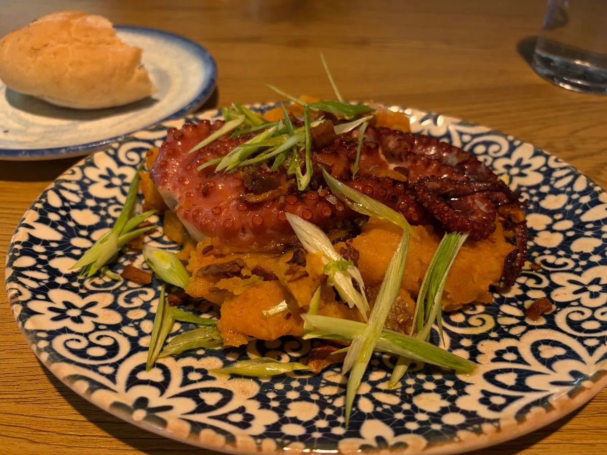 Pulpo a la gallega dressé sur planche de bois : rondelles de pomme de terre, morceaux de poulpe tendre saupoudrés de paprika fumé doux et fort, filet d'huile d'olive.
