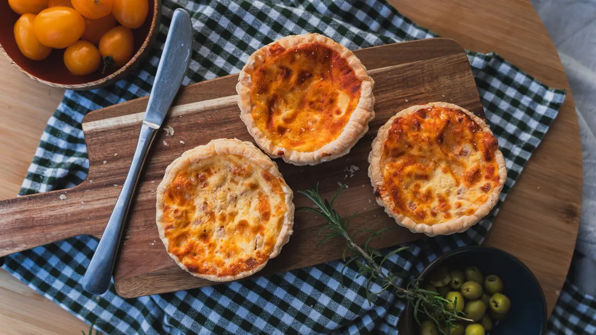 Quiche lorraine tiède à la pâte dorée, garnie de lardons fumés et de migaine crémeuse, part coupée sur assiette