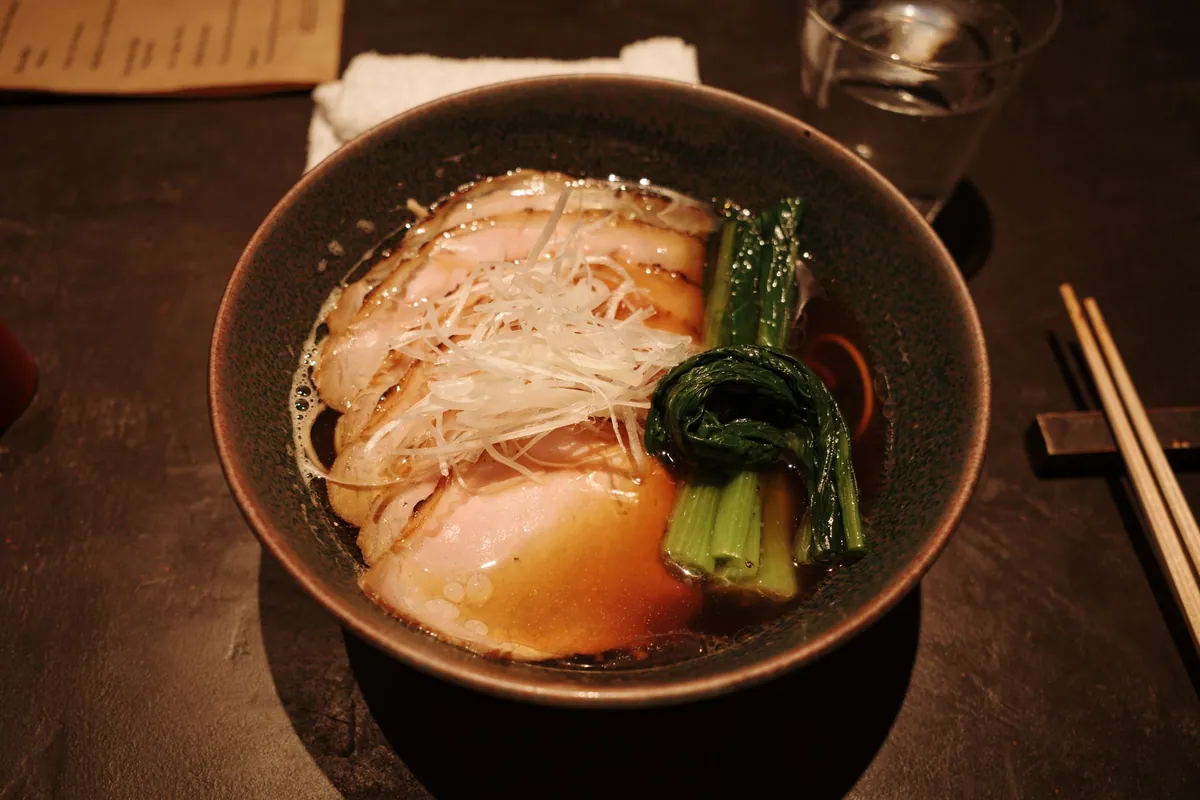 Bol de ramen shoyu avec nouilles, tranches de chashu, œuf ajitama mariné coulant, ciboule ciselée et feuille de nori dans un bouillon ambré fumant